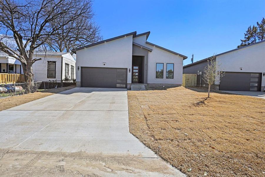 View of front facade with a garage, fence, driveway, and stucco siding