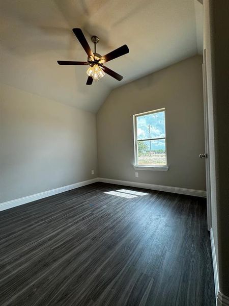 Unfurnished room featuring dark wood-type flooring, ceiling fan, and lofted ceiling