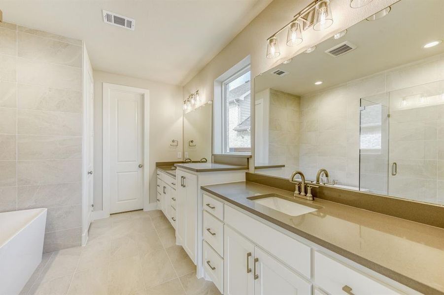 Bathroom featuring tile walls, two vanities, a freestanding tub, light tile patterned flooring, and a stall shower