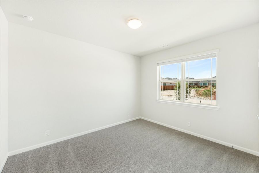 Empty bedroom with gray carpet, white walls, and a window overlooking the backyard