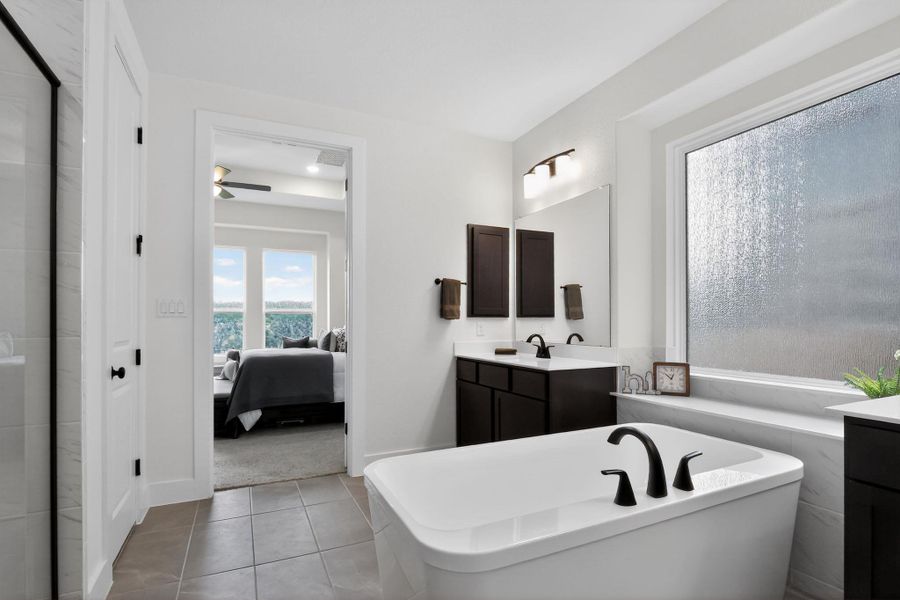 Contemporary bathroom featuring a freestanding tub with matte black fixtures, dual dark wood vanities with white countertops, a large privacy window, and tile flooring Contemporary bathroom featuring a freestanding tub with matte black fixtures, dual dark wood vanities with white countertops, a large privacy window, and tile flooring