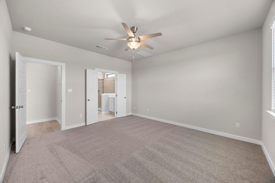 A spacious primary bedroom features soft carpeting, a ceiling fan, and private access to a well-appointed bathroom. A spacious primary bedroom features soft carpeting, a ceiling fan, and private access to a well-appointed bathroom.