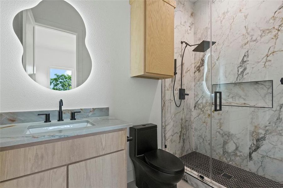 Bathroom featuring a marble finish shower, vanity, and a textured wall Bathroom featuring a marble finish shower, vanity, and a textured wall