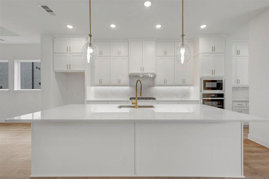 The kitchen features a spacious island with a white countertop, white cabinetry with gold-toned hardware, a gold-toned faucet, and built-in appliances including an oven and microwave