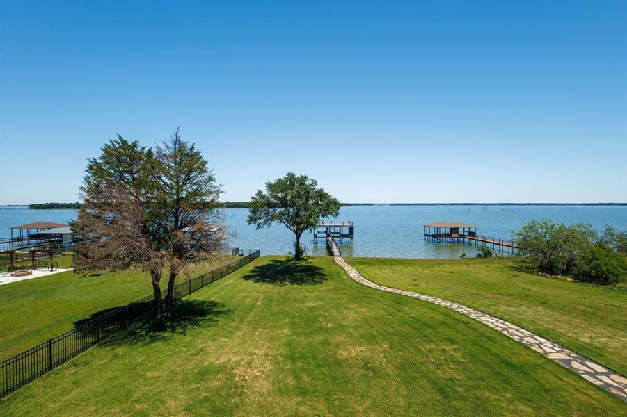 Expansive waterfront property featuring a manicured lawn, a winding stone path, mature trees, and multiple private boat docks extending into the water