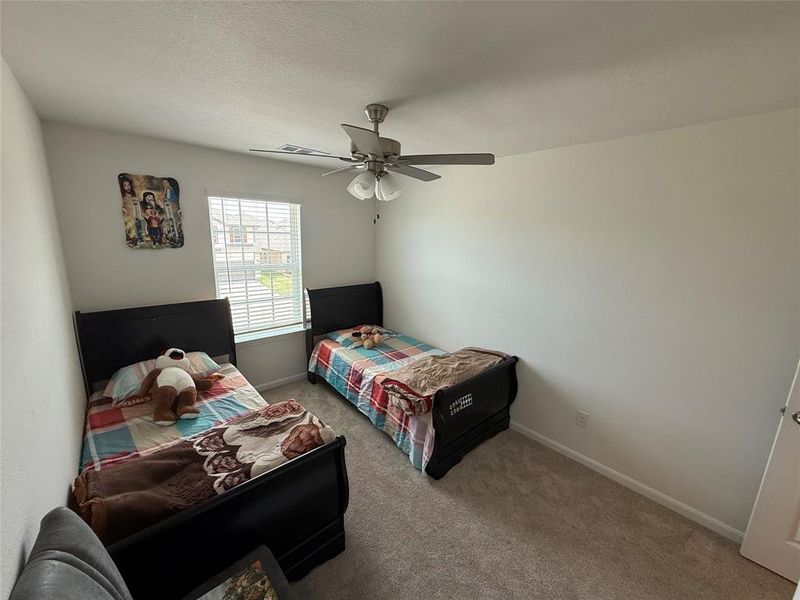 Bright room featuring a window with blinds, a ceiling fan with light fixture, light neutral-toned walls, and grey carpet flooring