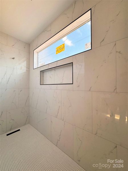 Luxurious shower with marble-style tile and sleek built-in niche.