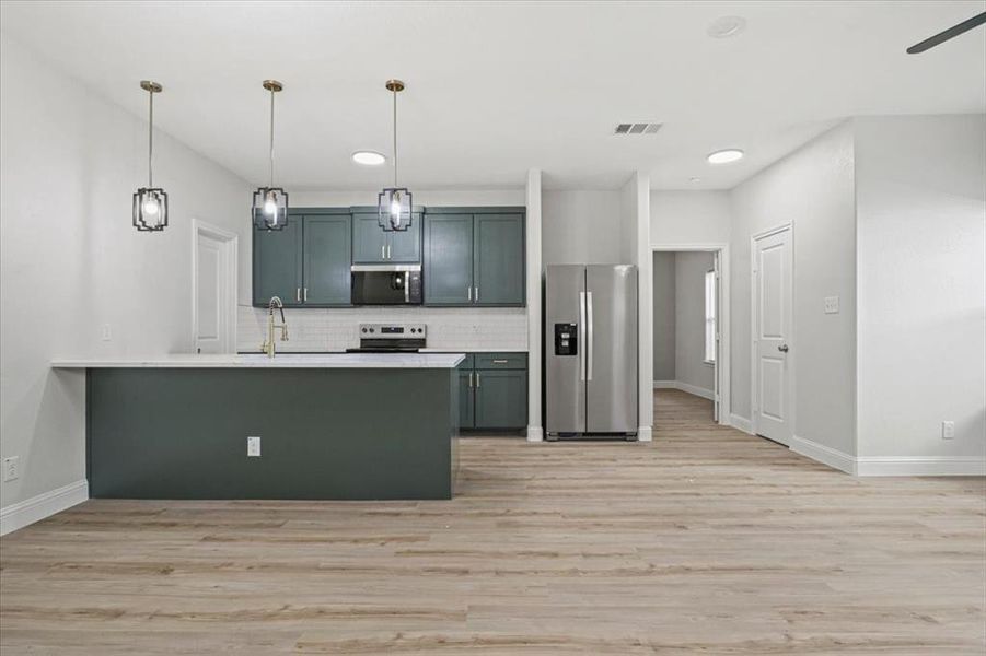 Kitchen with kitchen peninsula, appliances with stainless steel finishes, decorative backsplash, pendant lighting, and light hardwood / wood-style floors