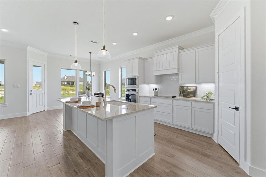 Modern kitchen featuring a large central island with a sink, pendant lighting, shaker-style cabinetry, stainless steel appliances, and wood-finish flooring