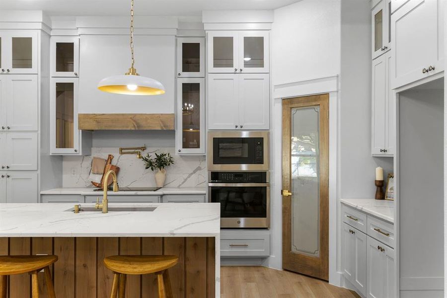 Kitchen with oven, white cabinets, hanging light fixtures, a breakfast bar, and light stone countertops