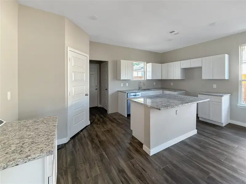 Kitchen with light stone counters, white cabinetry, a kitchen island, dark wood-type flooring, and stainless steel dishwasher