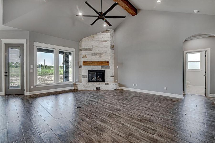 Unfurnished living room with ceiling fan, a fireplace, and lofted ceiling with beams