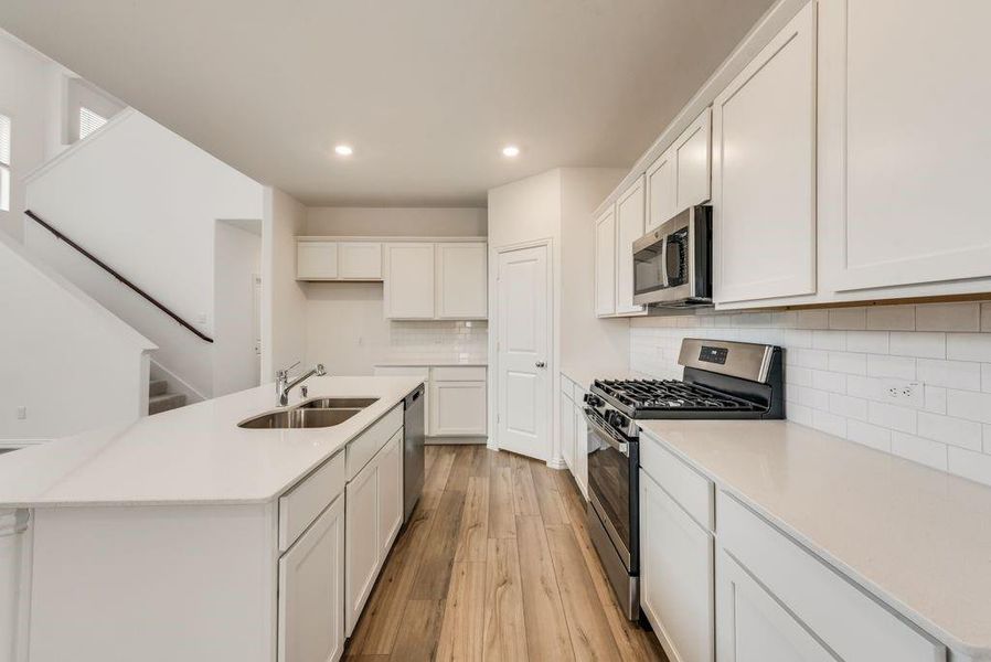 Kitchen featuring a center island with sink, stainless steel appliances, sink, light wood-type flooring, and white cabinets