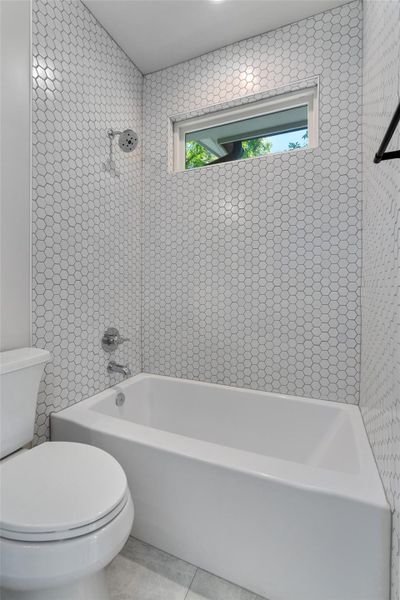 Full bathroom in secondary bedroom featuring a white ceramic bathtub, chrome shower fixtures, and white hexagonal tile walls Full bathroom in secondary bedroom featuring a white ceramic bathtub, chrome shower fixtures, and white hexagonal tile walls