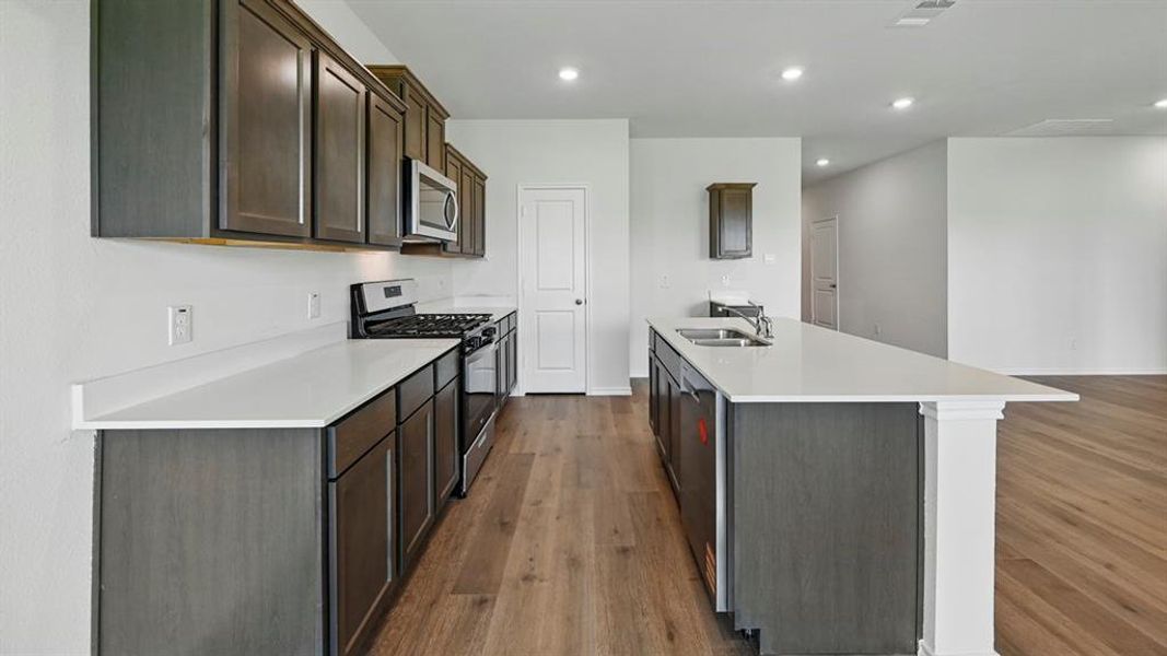 Kitchen featuring stainless steel appliances, recessed lighting, dark wood-type flooring, a kitchen island with sink, and dark brown cabinets