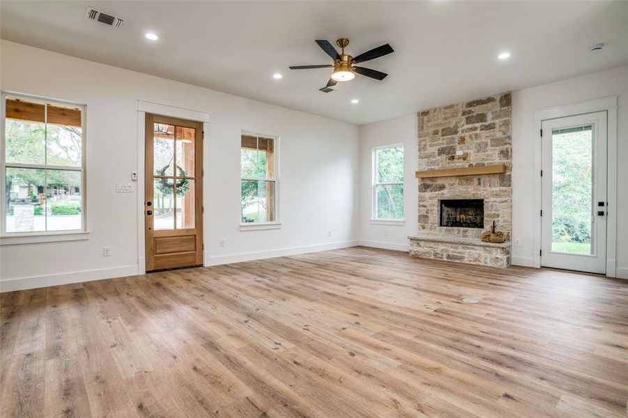 Unfurnished living room featuring a stone fireplace, ceiling fan, plenty of natural light, and light hardwood / wood-style flooring