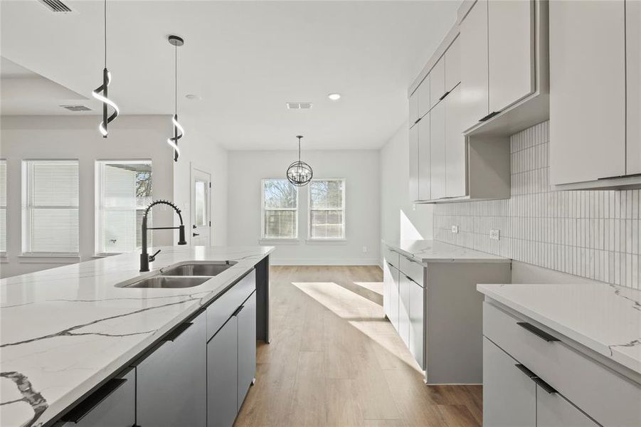 Kitchen with light wood-style flooring, visible vents, decorative backsplash, and a sink