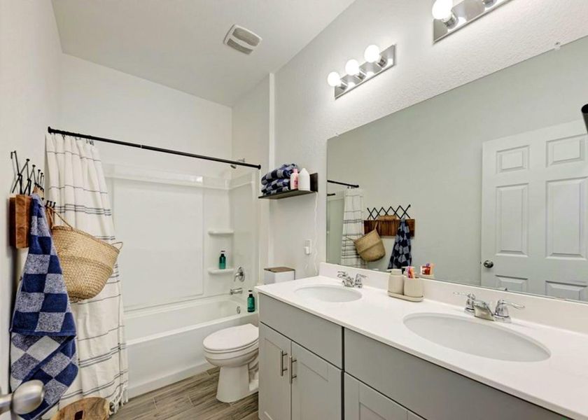 Bathroom featuring double vanity, shower / tub combo with curtain, and wood finish floors Bathroom featuring double vanity, shower / tub combo with curtain, and wood finish floors
