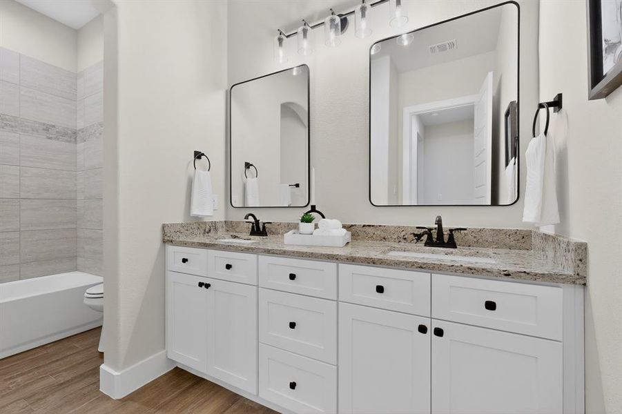 Dual sink vanity with white cabinetry, speckled countertop, and matte black fixtures