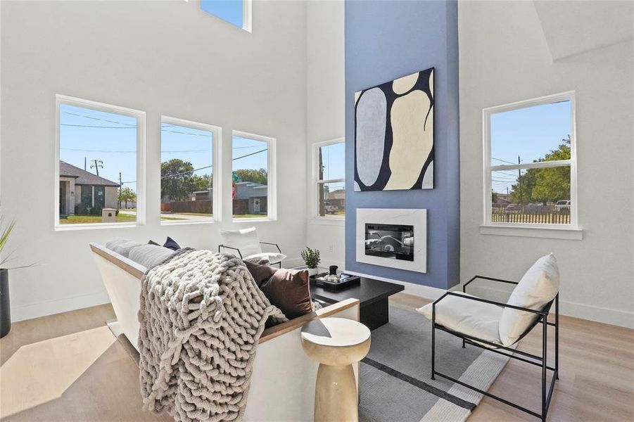 Living room with light wood-style flooring, a towering ceiling, and a glass covered fireplace Living room with light wood-style flooring, a towering ceiling, and a glass covered fireplace