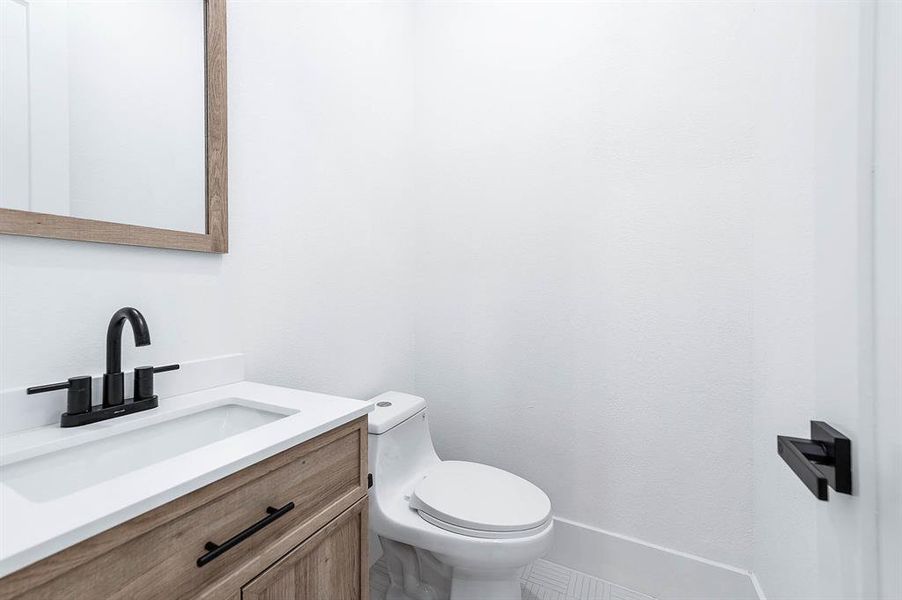 Modern half-bath with a clean, white interior, featuring a wooden vanity with a sleek sink and black faucet, a matching mirror, and a toilet. The bathroom has a minimalist design with contemporary fixtures.