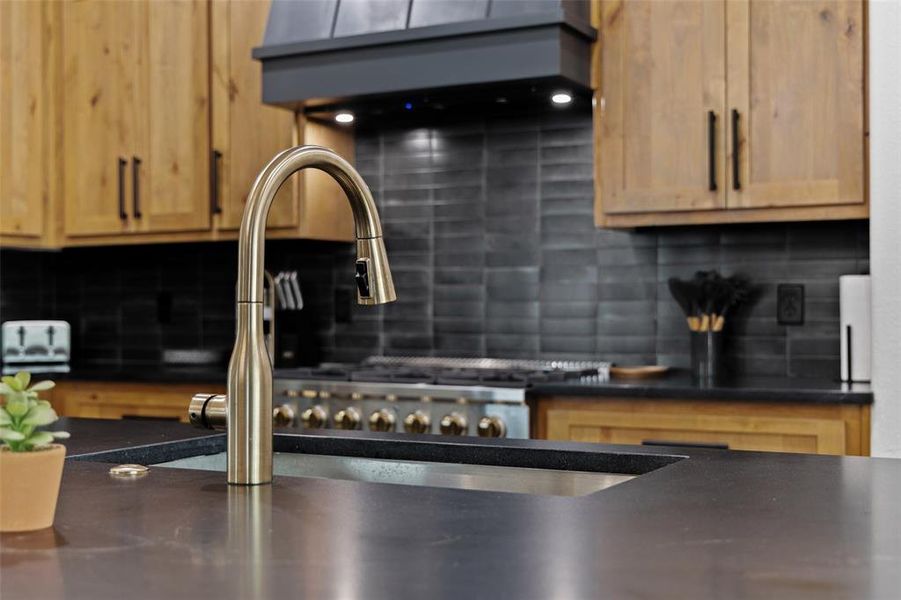 Kitchen view of tasteful backsplash, light wood finish cabinetry, and dark stone countertops