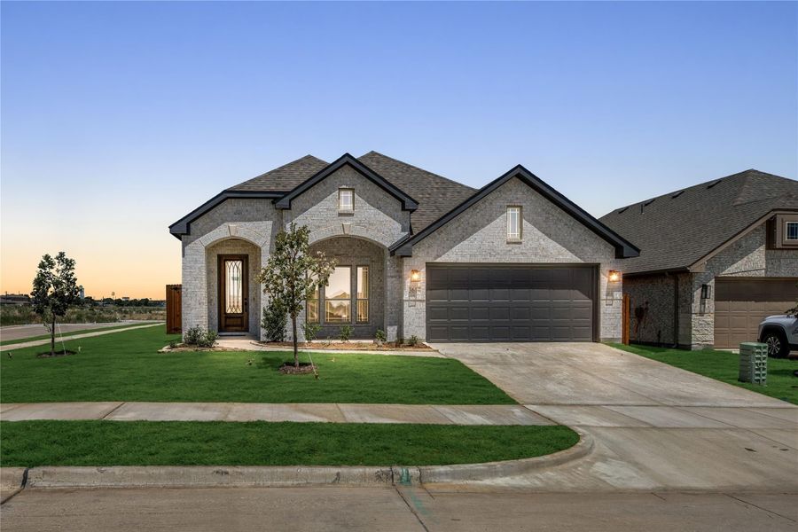 Single-story home with light brick exterior, arched entry, two-car garage, and manicured front lawn at dusk