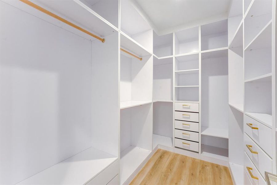 This large custom built closet features built-in drawers with gold accented hardware, storage space, and clothes hanging rods.