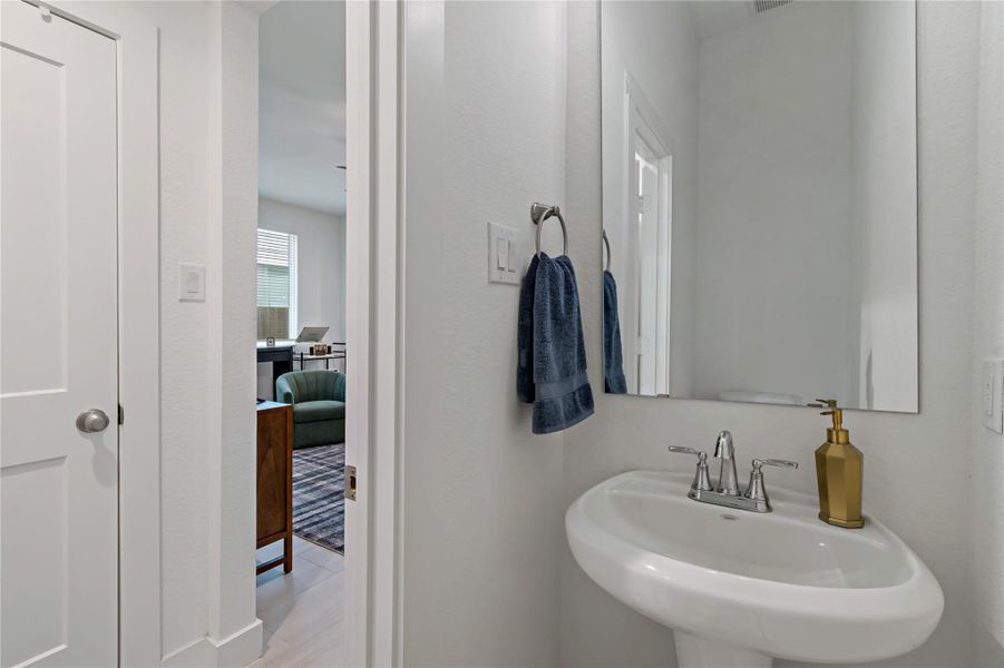 Stylish half-bathroom featuring a sleek pedestal sink, elegant fixtures, and ample natural light filtering through the adjacent room. Stylish half-bathroom featuring a sleek pedestal sink, elegant fixtures, and ample natural light filtering through the adjacent room.