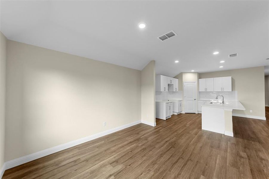 Open-concept living space featuring wood-finish flooring, recessed lighting, and a kitchen with white cabinetry, a kitchen island, and a sink with a gooseneck faucet