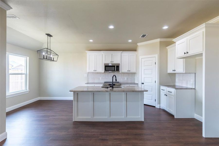 Kitchen featuring a central island with a black faucet, white shaker-style cabinetry, light-toned backsplash, and dark wood-finish flooring