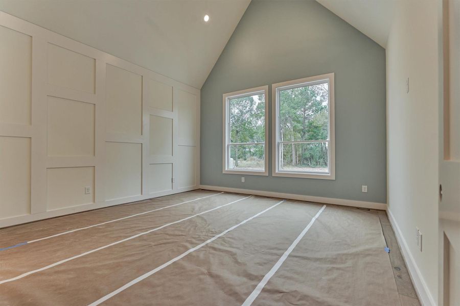 Serene primary bedroom with vaulted ceilings, accent wall paneling, and large picture windows offering peaceful views of the surrounding trees.