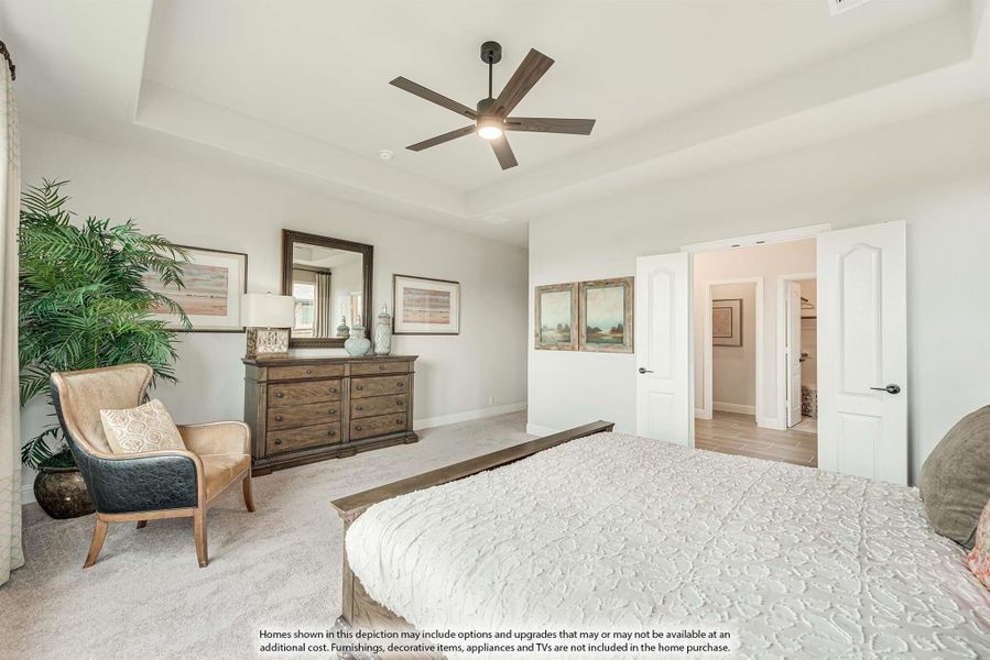Master bedroom with tray ceiling, ceiling fan, carpet flooring, and open door to ensuite bathroom and closet.