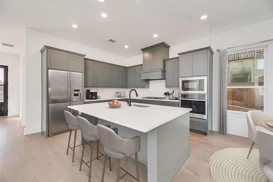 Kitchen with gray cabinets, built in appliances, light wood-style floors, a kitchen island with sink, and recessed lighting
