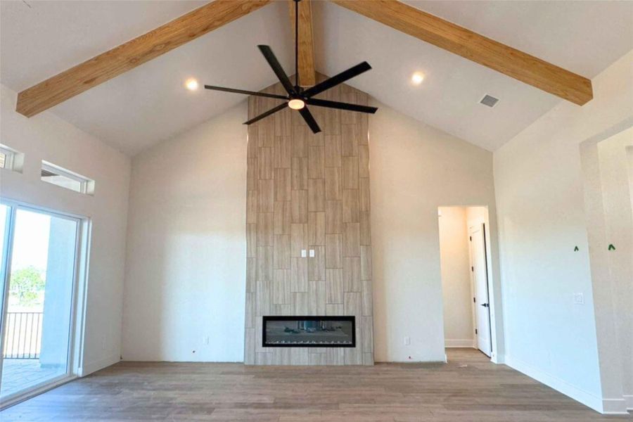 Unfurnished living room featuring high vaulted ceiling, beam ceiling, wood finished floors, a tile fireplace, and recessed lighting