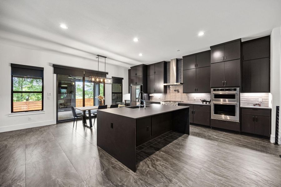 This modern kitchen features sleek dark custom cabinetry, a large dekton waterfall island with seating, stainless steel appliances, and ample natural light from large windows and glass doors. Perfect for entertaining and family gatherings. This modern kitchen features sleek dark custom cabinetry, a large dekton waterfall island with seating, stainless steel appliances, and ample natural light from large windows and glass doors. Perfect for entertaining and family gatherings.
