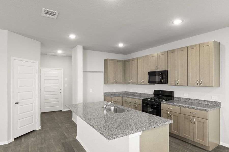 Image of a kitchen with granite countertops, a center island, black kitchen appliances, and light brown cabinetry