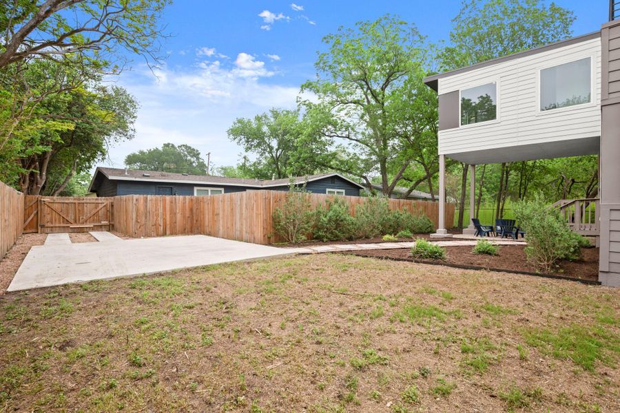 Private backyard featuring a modern two-story structure with white siding and gray accents, a concrete patio area, and a new wooden privacy fence with a gate