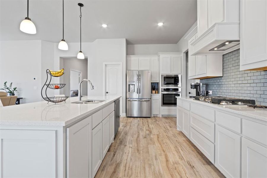 Kitchen featuring sink, light wood-type flooring, a kitchen island with sink, tasteful backsplash, and stainless steel appliances