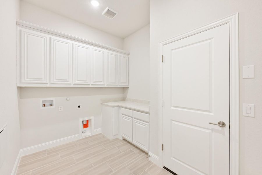 Laundry room with white upper cabinets, built-in counter, washer hookups, and light tile flooring