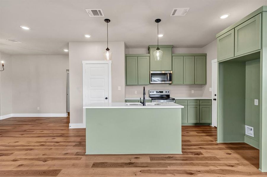 Kitchen featuring green cabinets, recessed lighting, decorative light fixtures, appliances with stainless steel finishes, and light wood-style floors