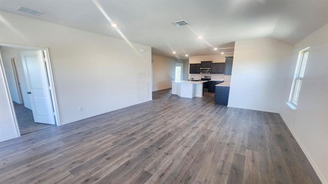 Spacious living area featuring wood-finish flooring, recessed lighting, white walls, and a window for natural illumination