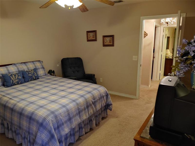 Carpeted bedroom featuring a ceiling fan with light fixture and a framed doorway opening to a hallway