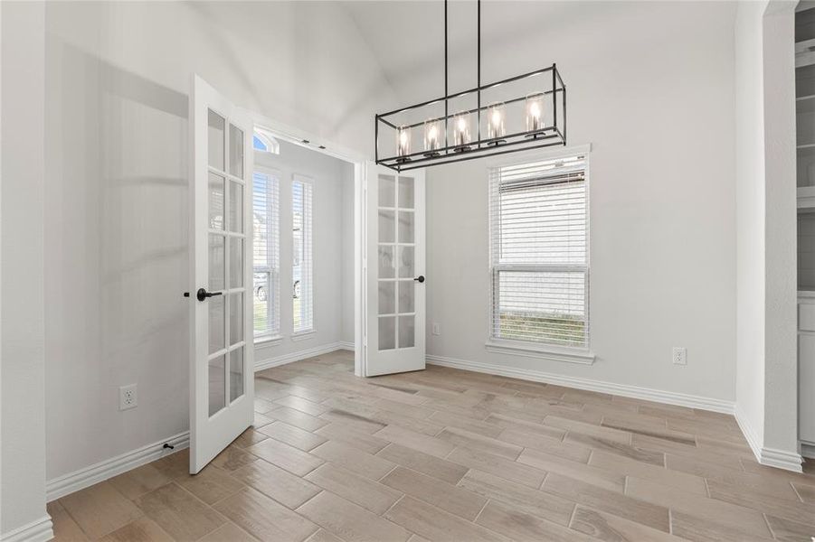 Unfurnished dining area with light hardwood / wood-style flooring, lofted ceiling, french doors, and a chandelier