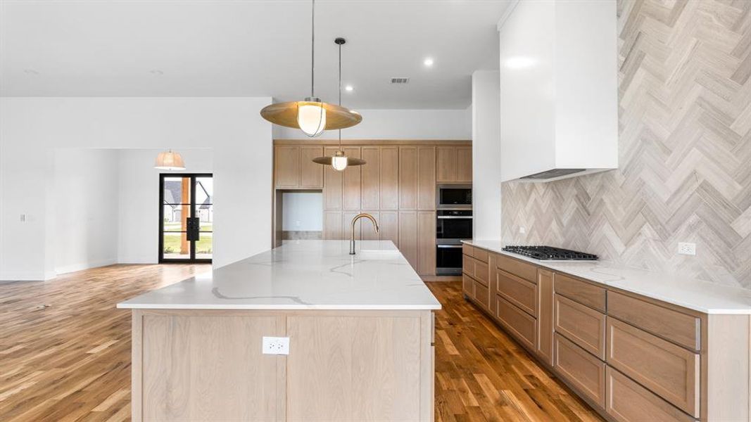 Kitchen featuring light wood-type flooring, light stone countertops, stainless steel appliances, and decorative light fixtures