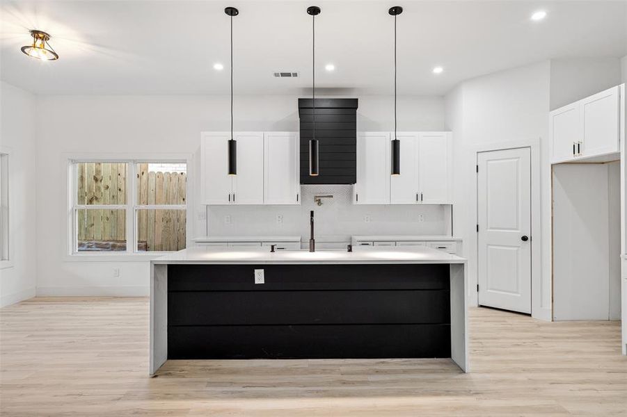 Kitchen featuring hanging light fixtures, light hardwood / wood-style floors, white cabinetry, and a kitchen island with sink