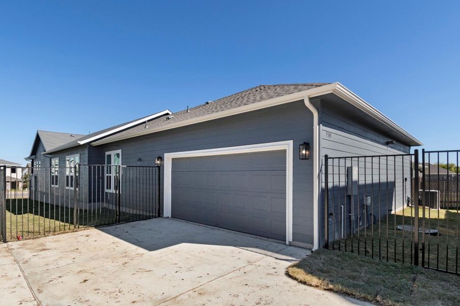 View of side of property featuring driveway, a garage, roof with shingles, and a gate