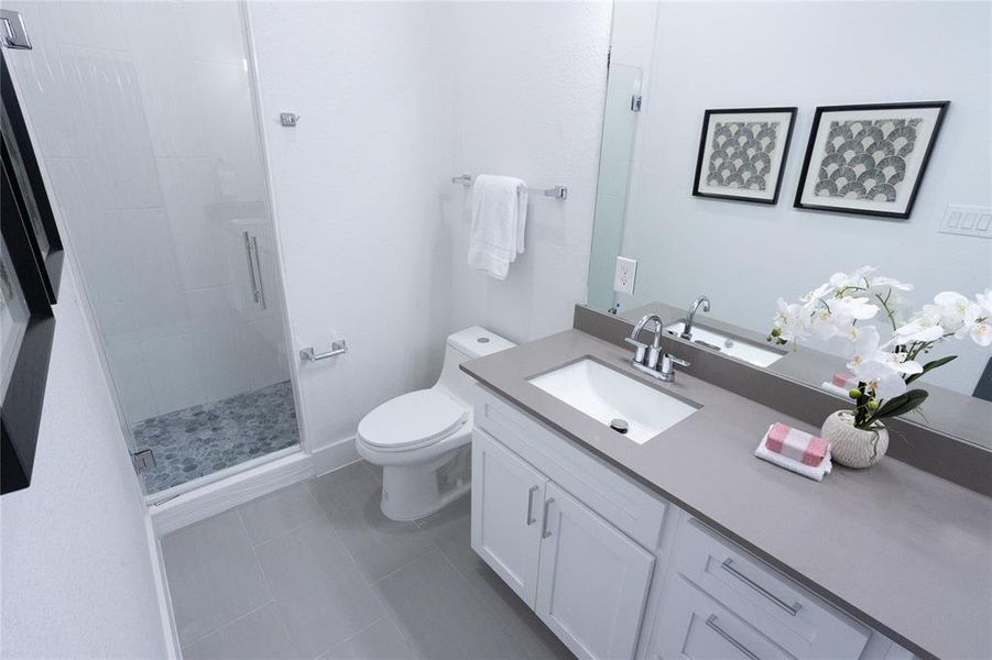 Bathroom featuring tile patterned floors, vanity, toilet, and a shower with door