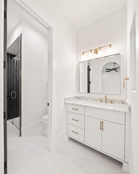 White tile flooring complementing a vanity with a light-toned countertop, brass hardware, and a framed mirror