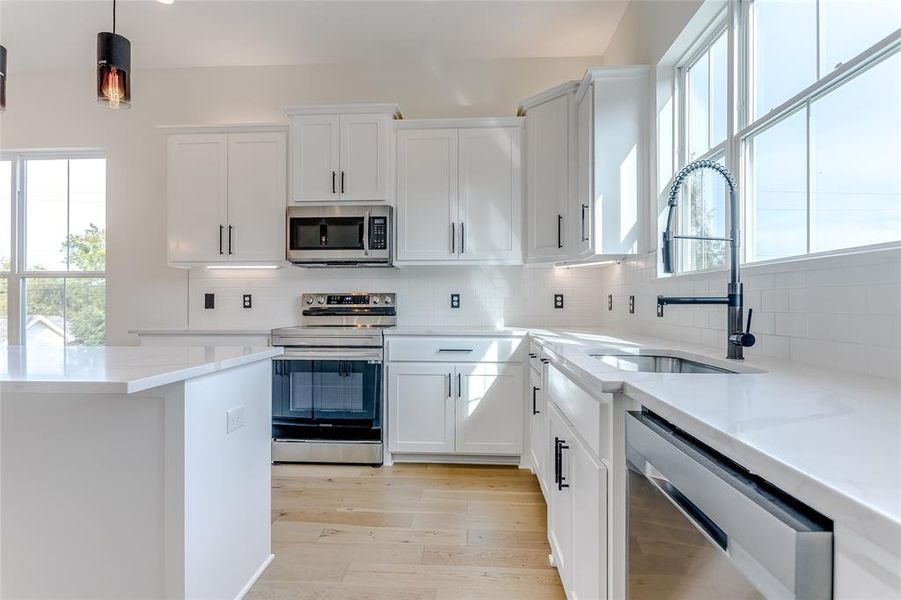 Kitchen featuring appliances with stainless steel finishes, tasteful backsplash, white cabinetry, and a wealth of natural light